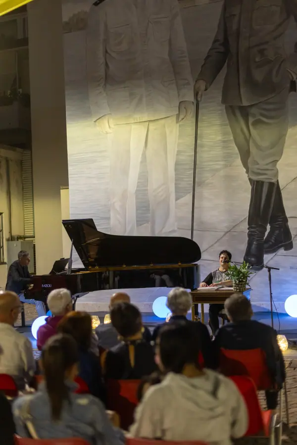 Il pubblico in ascolto davanti al palco, con il pianoforte a coda sotto un grande telo bianco.