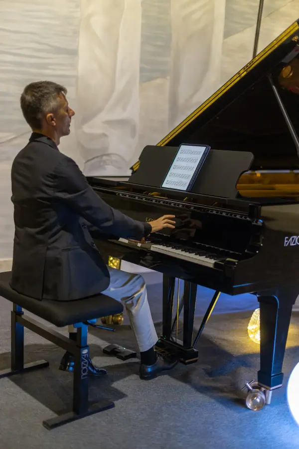 Il pianista suona il pianoforte a coda, rischiarato da una sfera di luce bianca.