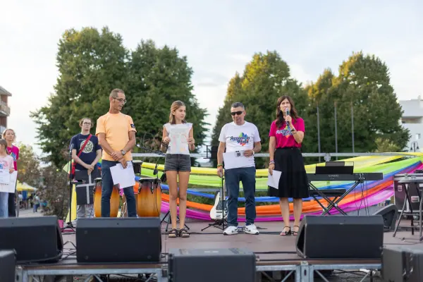 Secondo posto: sul palco, una ragazza mostra il suo disegno su un grande foglio bianco, tra gli organizzatori e i nastri colorati.