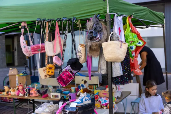 Una bancarella sotto un gazebo verde, con borse, peluche e scarpe appese e disposte sul tavolo.