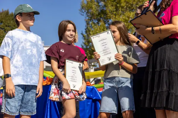 Ragazzi sul palco con gli attestati in mano, mentre la presentatrice consegna l'ultimo.