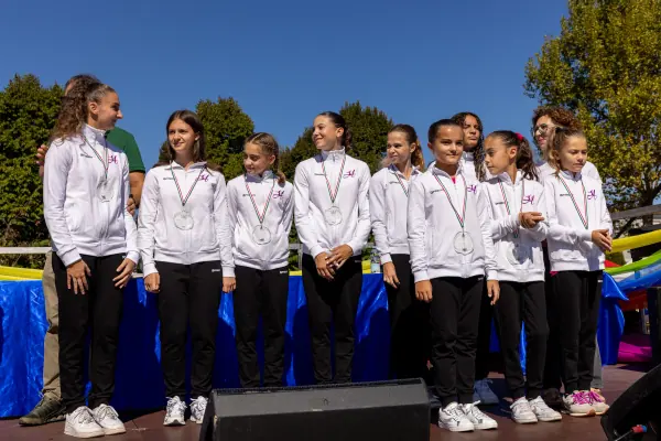 Una squadra di ginnaste in tuta bianca, in fila sul palco con le medaglie al collo.
